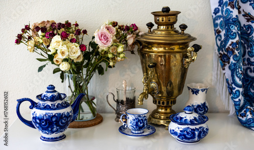 A still life photo of a copper Russian samovar, rose bouqet and painted blue teaset
