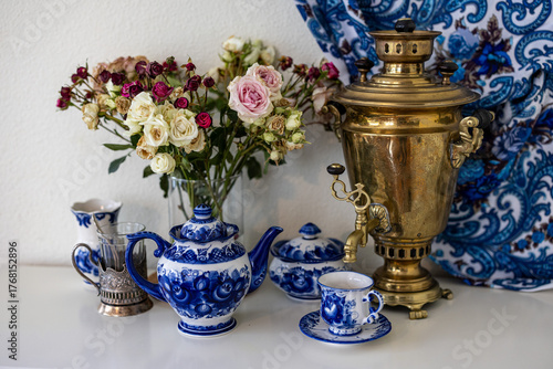 A still life photo of a copper Russian samovar, rose bouqet and painted blue teaset