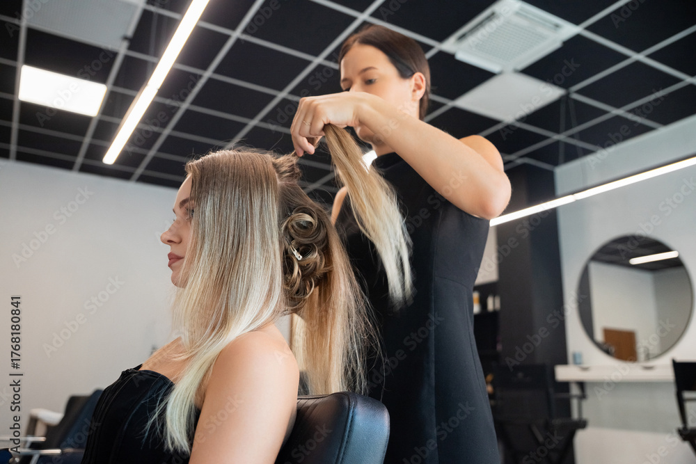 Fototapeta premium Stylist creating an elegant hairdo for a client in a modern salon during a lively afternoon appointment