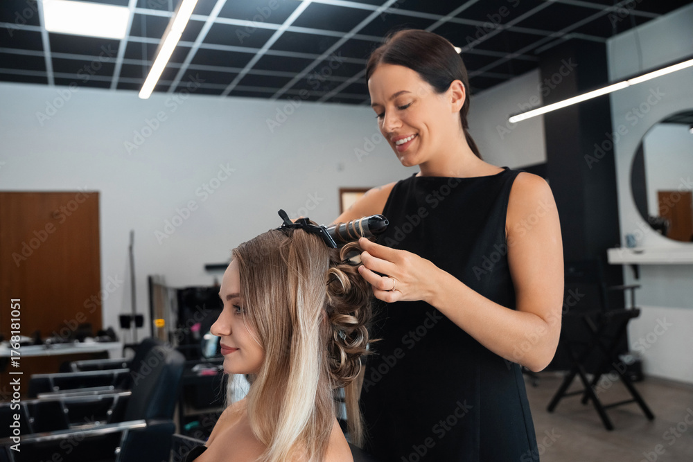 Fototapeta premium Hair stylist curling hair for a client at a modern salon during mid-afternoon