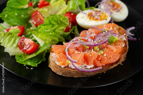 Delicious healthy breakfast - boiled egg, sandwich salmon and green salad. Balanced meal plate on dark background