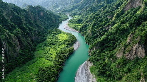 Aerial view of a winding turquoise river flowing through a lush green mountainous valley during daylight with vibrant vegetation and clear skies