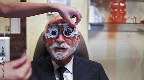 Professional optometrist examining a senior patient's vision with a phoropter trial frame during an appointment in the ophthalmology clinic, selecting the correct lenses for prescription glasses