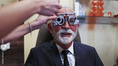 Professional optometrist examining a senior patient's vision with a phoropter trial frame during an appointment in the ophthalmology clinic, selecting the correct lenses for prescription glasses