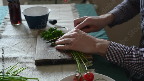 A man is chopping green parsley on a wooden board.