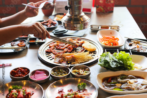 Korea BBQ style restaurant. Asian traditional pickle vegetable ingredients on table with people grilling background.
