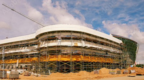 Construction of a modern stadium in a sunny location, showcasing scaffolding and heavy equipment