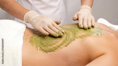 Upper Back Mud Mask Treatment by Therapist Wearing Gloves in Beauty Salon with White Background Applying Skincare Cream in Spa Center to Young Woman for Relaxing Wellness Treatment