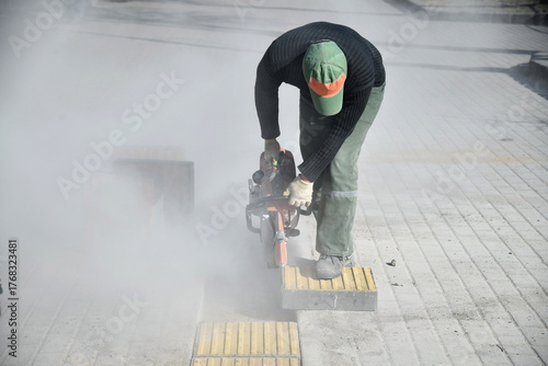Fotografi A worker is sawing a road curb, there is a lot of dust.