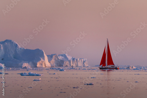 A solitary red sailboat courageously navigates through the surreal, glacial landscape of Greenland's Ilulissat Icefjord