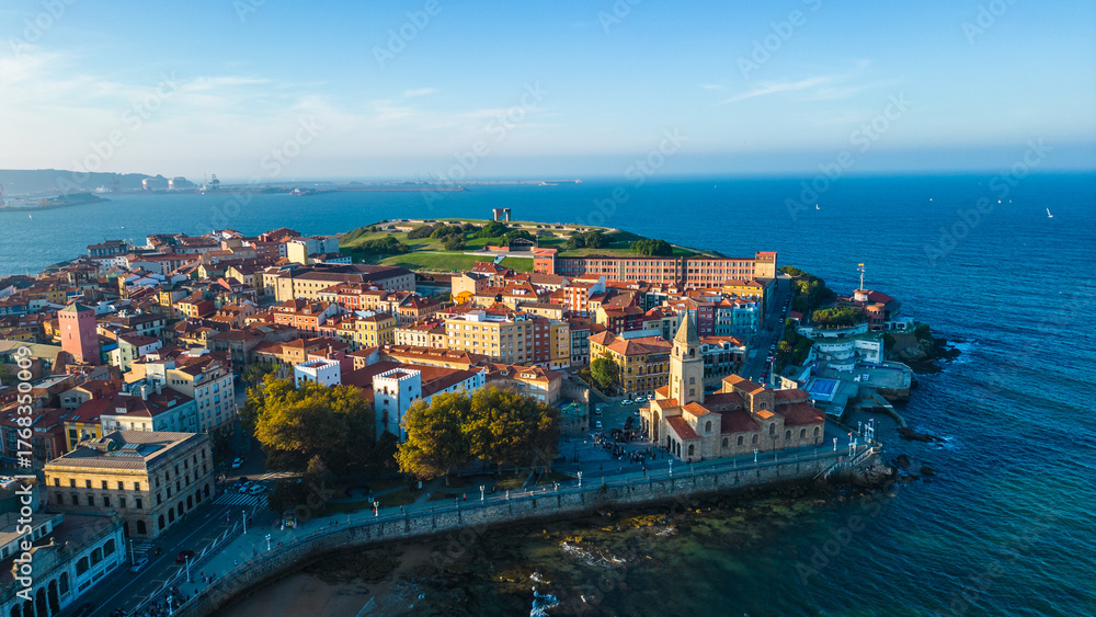 Obraz premium An aerial view captures the vibrant coastal city of Gijon, Spain, showcasing its historic architecture, bustling promenade, and the deep blue waters of the Cantabrian Sea.