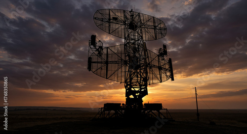 Modern military radar with large rotating antenna in open terrain at sunset.
