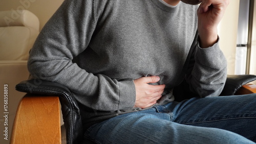 A man sitting in an armchair clutches his belly due to stomach ache