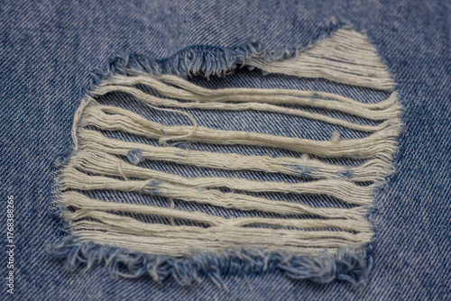 A close-up detail of blue jeans with a fashionable rip and white threads, showcasing the denim texture