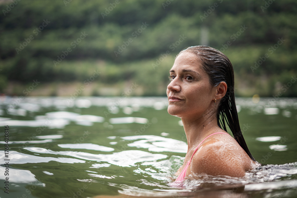 Fototapeta premium Serene woman swimming in a lake surrounded by nature, enjoying a peaceful moment of relaxation and connection with the outdoors on a summer day