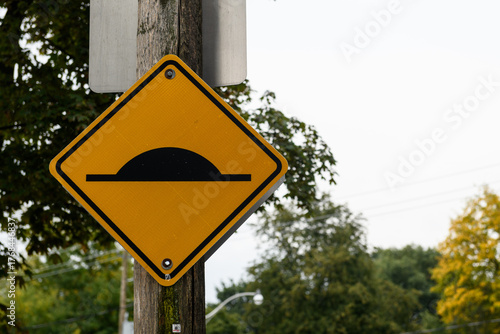 Photography Yellow traffic warning sign cautioning drivers to slow down because the road contains a speed bump or speed hump ahead