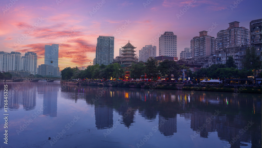 Fototapeta premium A traditional Chinese pagoda standing by the riverside amid modern high-rise buildings in Chengdu, China. The sunset sky adds warmth to the balance between old and new