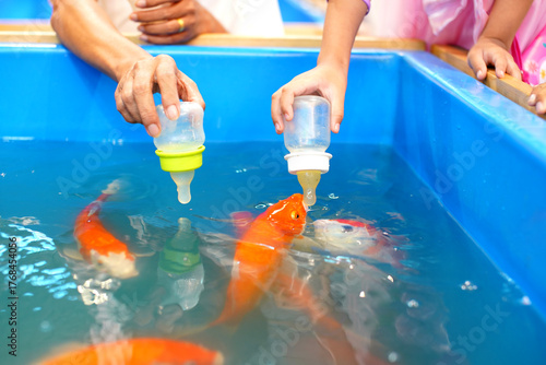 A child feeds vibrant koi fish using a bottle in a bright blue tank, capturing a tender moment of connection between humans and nature.