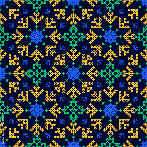 Seamless cross-stitch pattern with geometric folk motifs in yellow, green, and blue on a dark blue background.