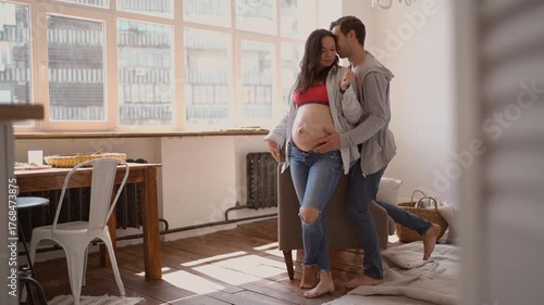 Pregnant wife and loving husband cuddling at home sharing smiles and baby dreams with tender embraces of her belly. man lovely kisses his wife. love and tenderness moments