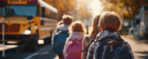 Children in colorful backpacks walk towards a school bus on a sunny autumn day