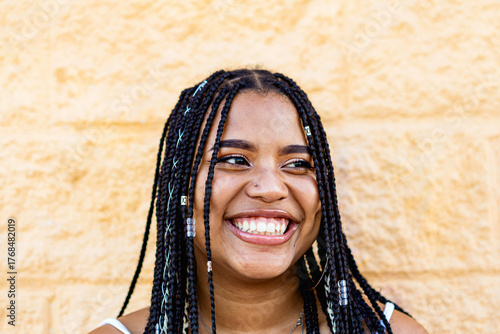 Portrait of a beautiful black woman with braids smiling with a yellow wall