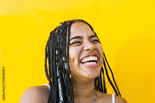 Portrait of a beautiful black woman with braids laughing with a yellow background