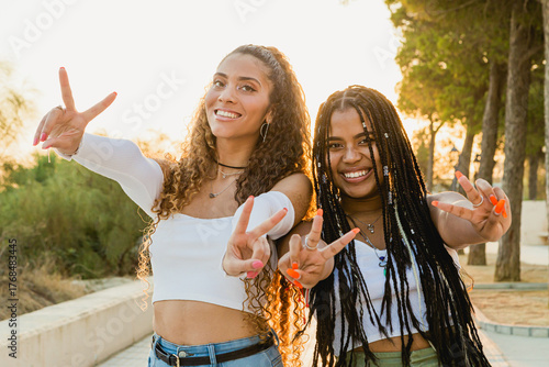 Portrait of a beautiful multiracial woman making victory sign on the street with the sunset behind her