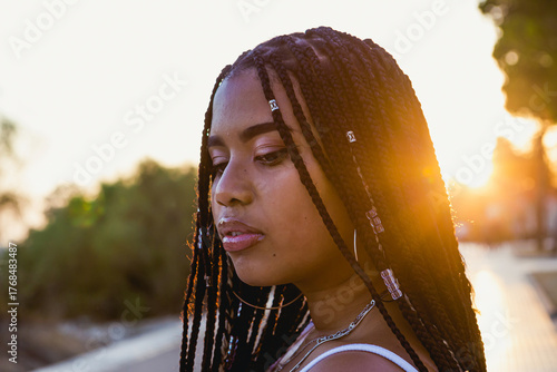 Portrait of a beautiful latin woman with braids on the street with the sunset behind her