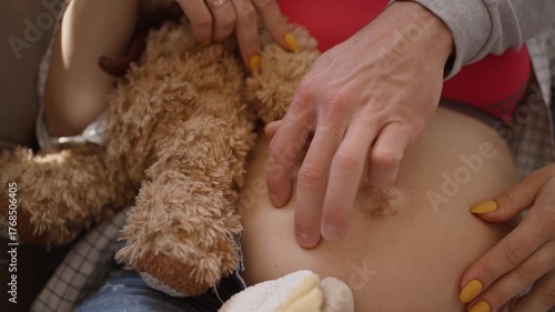 Loving husband and pregnant wife lying together on the couch, smiling while playing with baby shoes on her belly. Warm and emotional family moment. close up mans fingers on woman