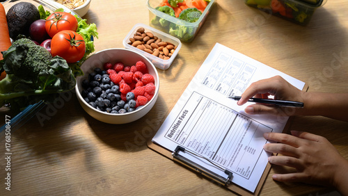 Nutritionist writing a healthy meal plan with fresh fruits, vegetables, and nuts on the table