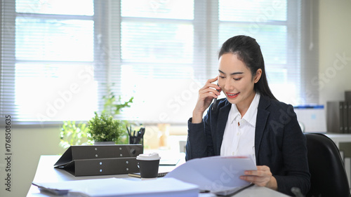 Tableau sur toile Businesswoman talking on the phone while reviewing documents at her desk, showin