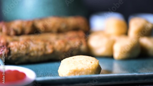 Crispy fried chicken wings, chicken nuggets and beef kebab in a plate. Kebab is Dipped into a Ketchup Bowl on a Table with Black Background a Macro Shot in 4K.