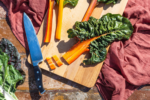 Overhead view of fresh organic colorful chard on earthy soil with cutting board and knife