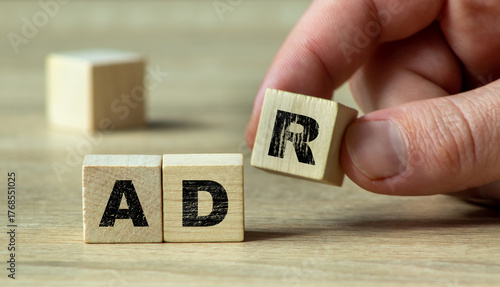 A hand is rearranging wooden blocks displaying the letters A, D, and R on a wooden surface. This image reflects creativity and problem-solving in a workspace. 