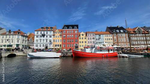 07 August, 2024, Copenhagen city center, Denmark Summer day scenic canal with boats and tourists, cyclists riding along colorful buildings and waterfront, vibrant urban atmosphere in European capital