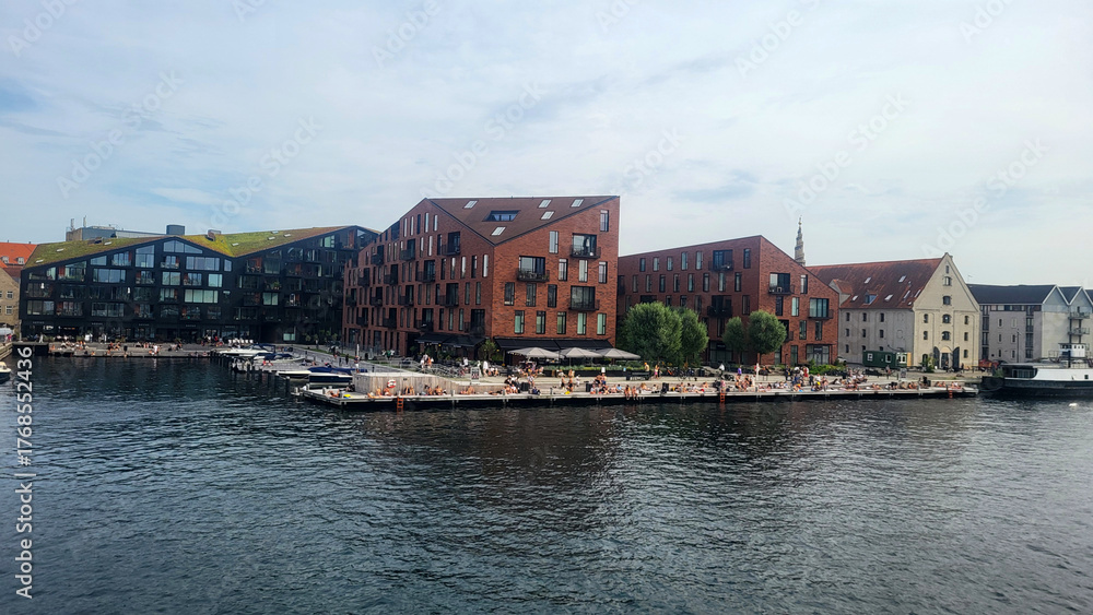 Obraz premium 07 August, 2024, Copenhagen city center, Denmark Summer day scenic canal with boats and tourists, cyclists riding along colorful buildings and waterfront, vibrant urban atmosphere in European capital
