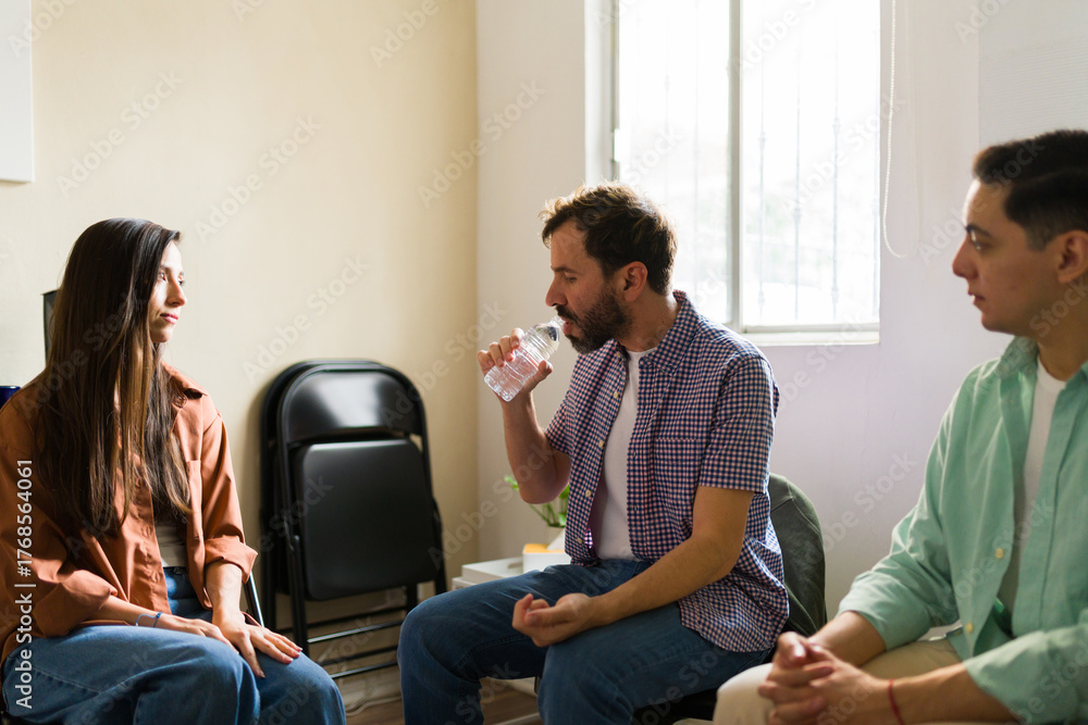 Fototapeta premium Distressed man drinking water to calm himself while attending group therapy meeting for support