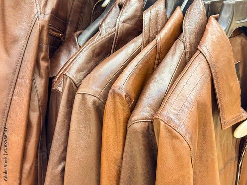A collection of brown leather jackets hanging on a rack. The jackets are neatly arranged, showcasing their texture and color.