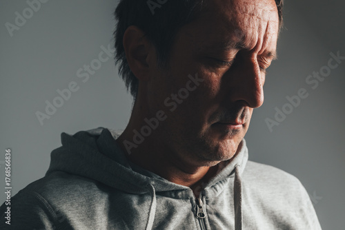 Billede på lærred Low key portrait of mature man in casual clothing with eyes closed, expressing regret, sadness, and emotional reflection