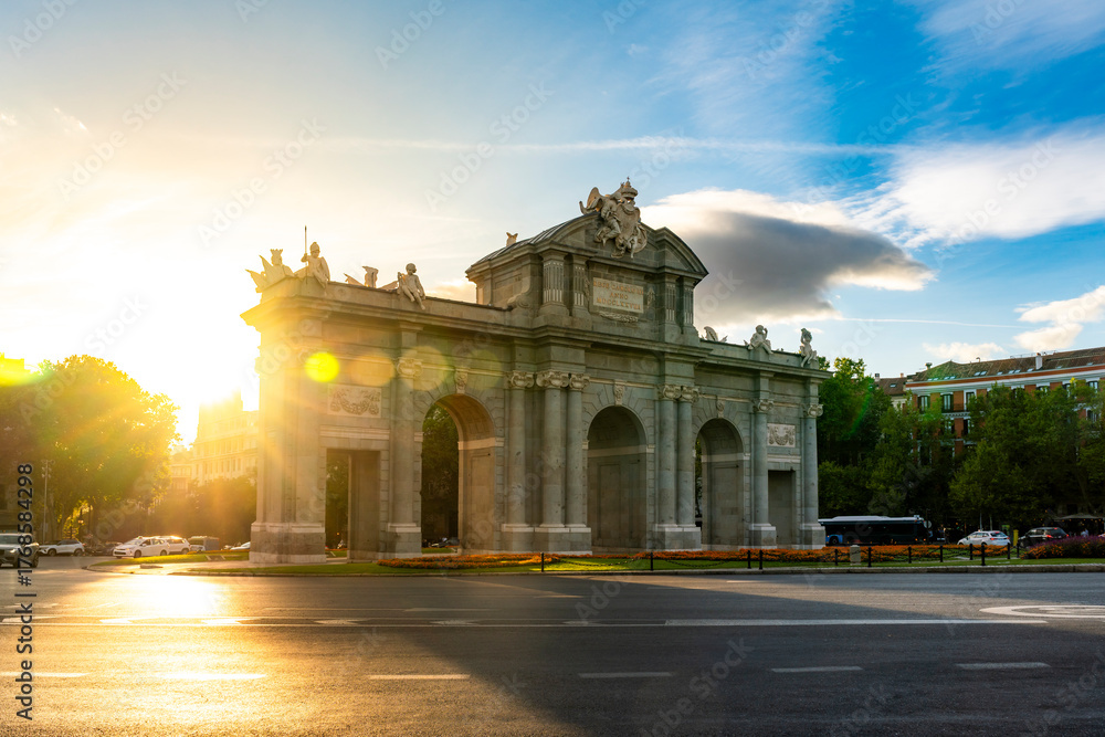 Obraz premium Puerta de Alcalá is bathed in golden sunset light in Madrid, Spain. The soft backlighting, lens flare, long shadows give the neoclassical monument a warm romantic atmosphere Plaza de la Independencia
