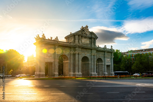 Puerta de Alcalá is bathed in golden sunset light in Madrid, Spain. The soft backlighting, lens flare, long shadows give the neoclassical monument a warm romantic atmosphere Plaza de la Independencia