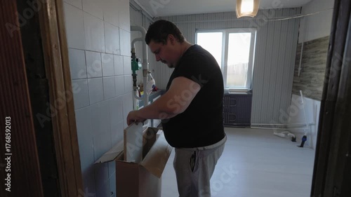 Male homeowner unpacking and preparing to assemble a new piece of kitchen furniture during a home renovation project. Diligent craftsman working on installing a modern cabinet.