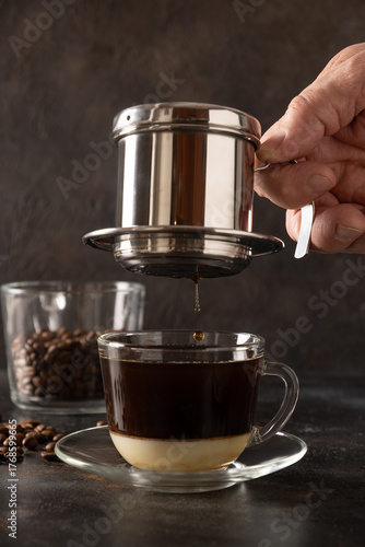 Brew Vietnamese coffee with sweet condensed milk in glass cup by traditional method on black background. Close up.