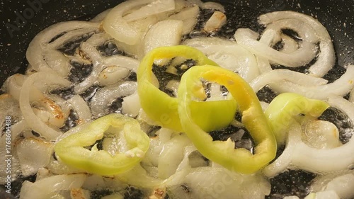 White onion rings and yellow peppers fried in a pan with vegetable oil. Medium shot.