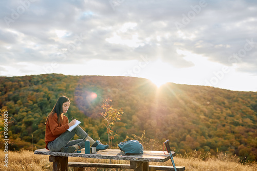 Obraz na płótnie Young woman journaling on a picnic table amidst autumn foliage during golden hou