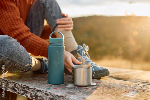 Принти на полотні Woman sitting on a wooden surface, holding a hot steamy metal mug while a water