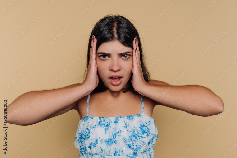 Fototapeta premium Young woman in floral dress holding her head in frustration.