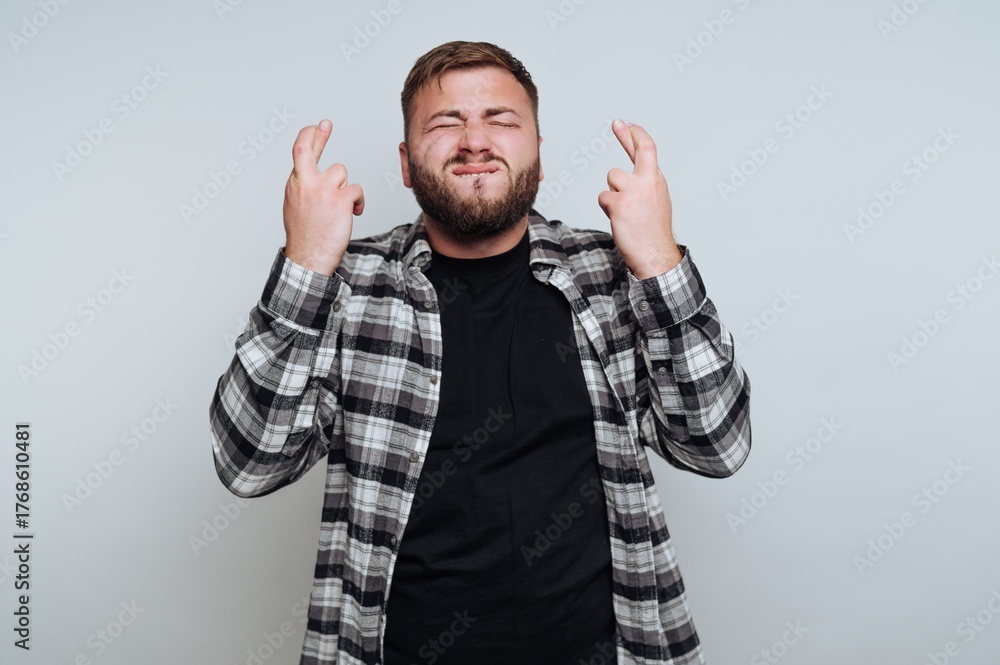 Naklejka premium Man with beard crossing fingers, wearing plaid shirt, hopeful expression.