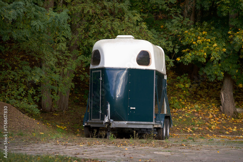 A horse trailer standing against a background of trees.